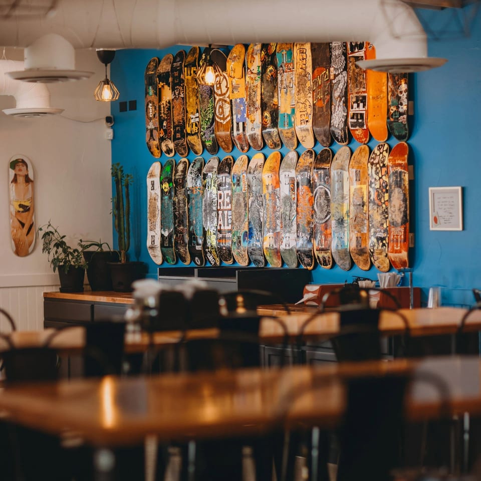 Shreddy's Tacos dining area with a blue wall adorned with numerous skateboards, and wooden tables.