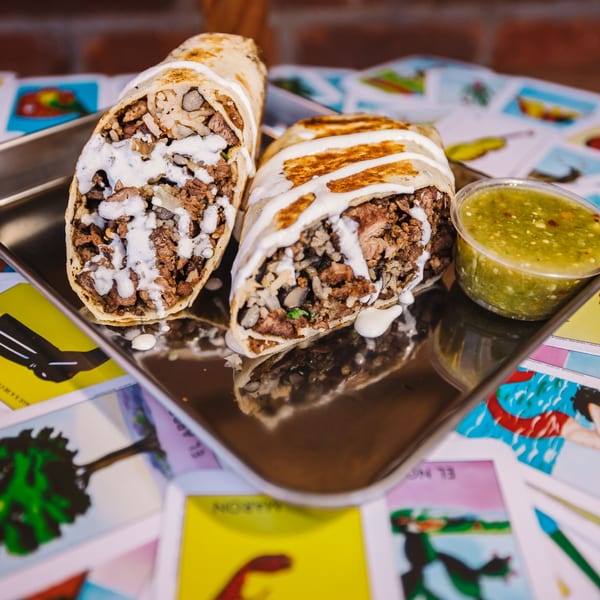Two Shreddy's Tacos burritos, cut in half, drizzled with white sauce, and a side of green salsa.