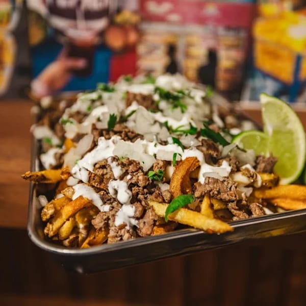 Shreddy's Tacos carne asada fries with sour cream, onions, cilantro, and lime wedges.