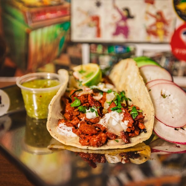 Shreddy's Tacos al pastor taco with lime, cilantro, and sauce, served with radishes and salsa.