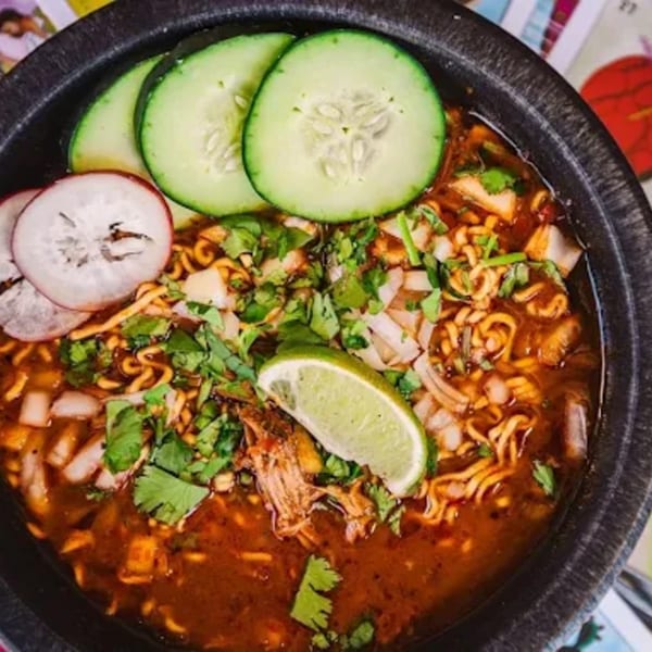 Shreddy's Tacos birria ramen with shredded meat, cilantro, onions, lime, cucumbers, and radishes.
