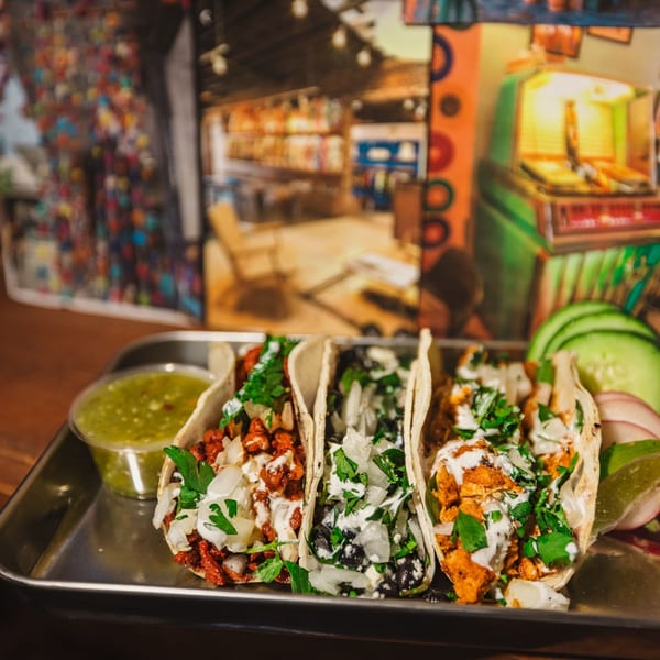 Three Shreddy's Tacos with various fillings, salsa verde, and garnishes on a metal tray.