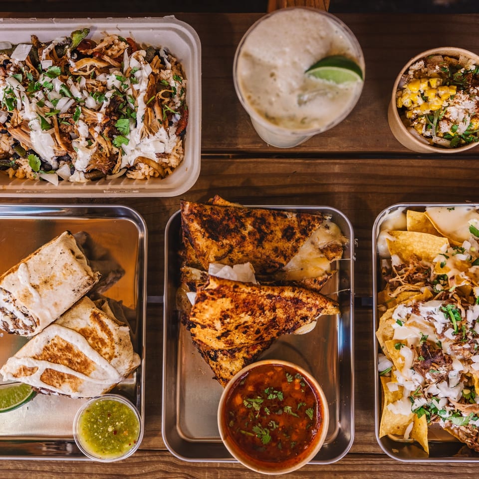 Overhead view of Shreddy's Tacos spread: burritos, quesadillas, nachos, elote, and a drink.