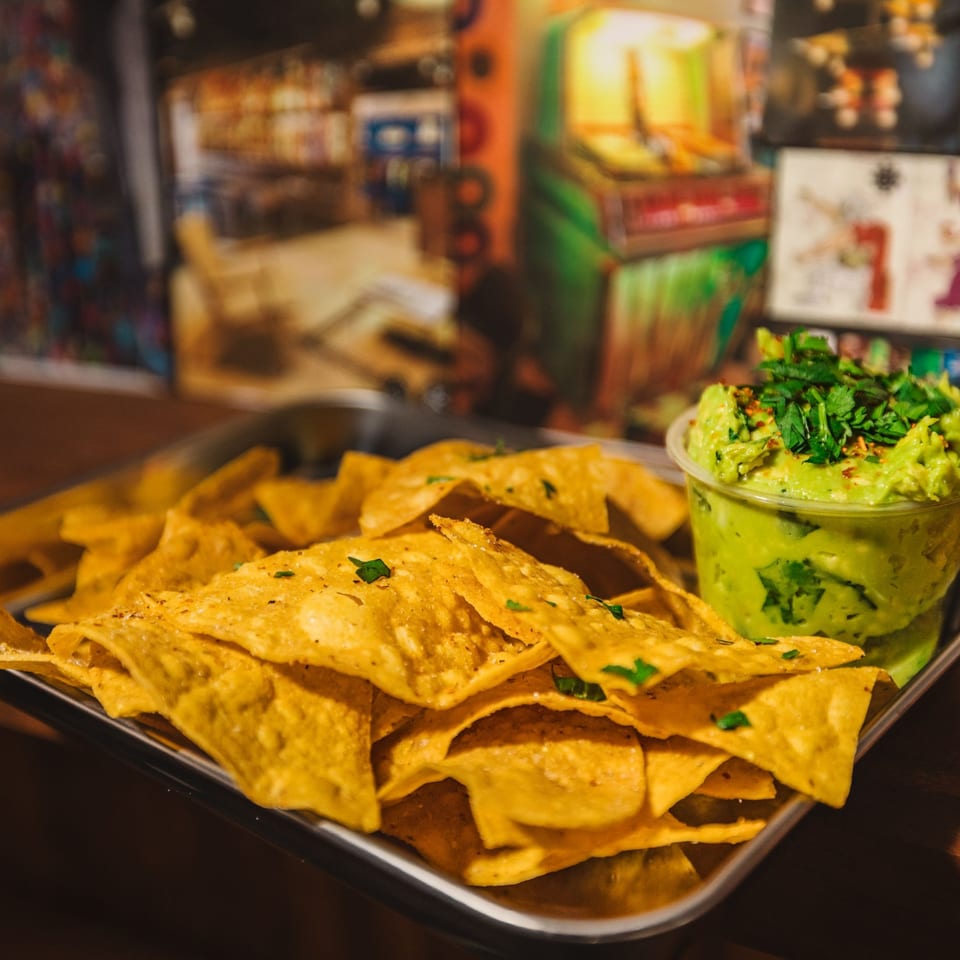 A metal tray filled with crispy tortilla chips and a side of Shreddy's guacamole.