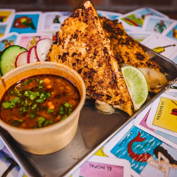 Shreddy's Tacos birria tacos with consommé, lime, cucumber, and radishes on a metal tray.