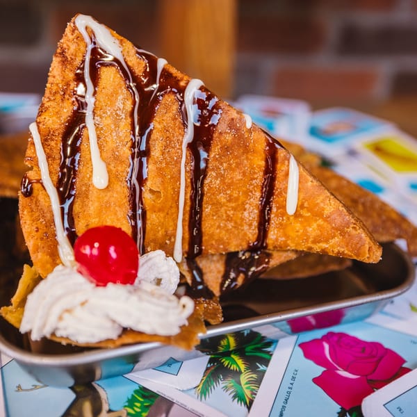 A dessert taco, drizzled with chocolate and white sauce, topped with whipped cream and a cherry.