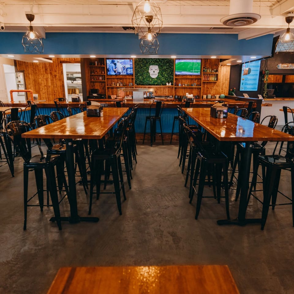Interior of Shreddy's Tacos with high-top tables, bar seating, and a skull logo on a green wall.